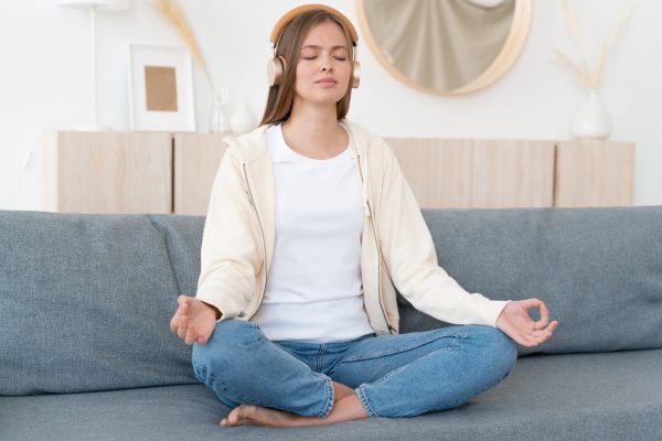 Calm young woman sitting on couch, practicing meditation yoga with mudra hands