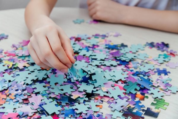 Caucasian girl collects puzzles on the table.